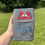 Gray Comfort Colors pocket t-shirt featuring a red crab applique peeking above the pocket with a personalized embroidered monogram stitched across the pocket, coastal beach-themed apparel.