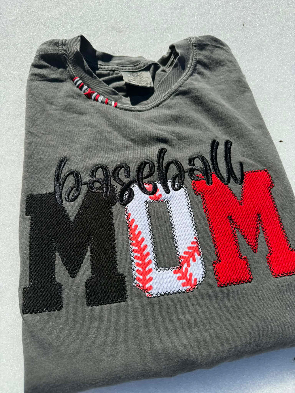 Folded gray t-shirt with 'Baseball Mom' text and baseball design on a light background