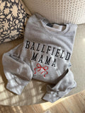 Gray sweatshirt with 'Ballfield Mama' text and red bow graphic on a textured surface.