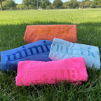 Folded Comfort Colors 1717 embroidered Mama t-shirt displayed on grass featuring oversized tonal embroidery lettering in a minimalist custom mom shirt design.