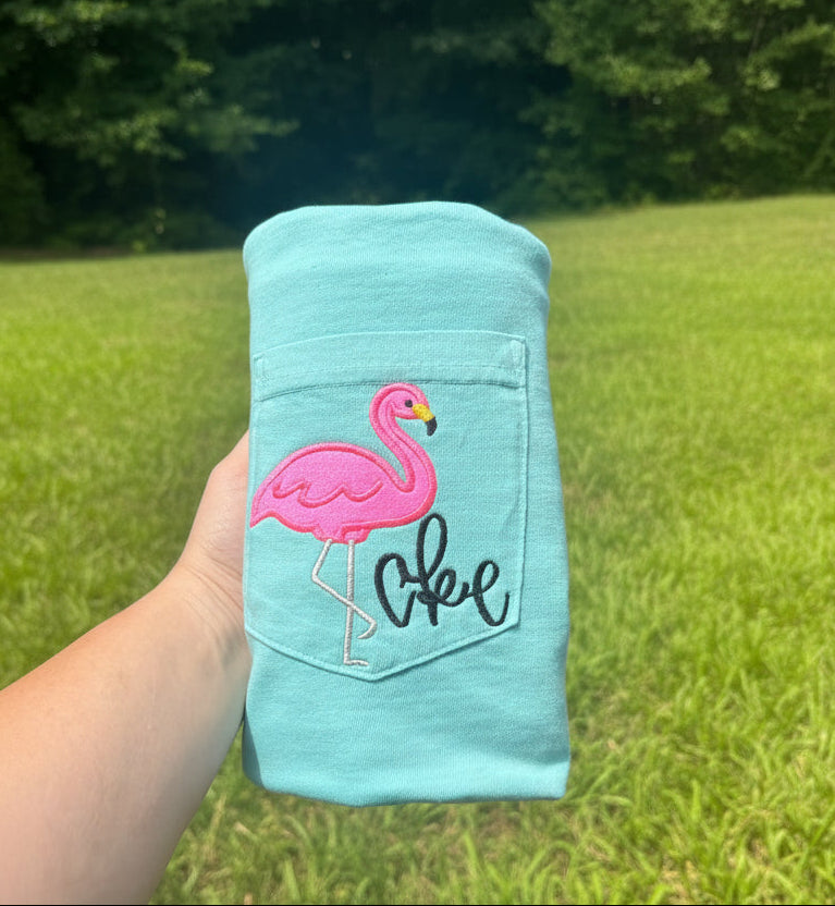Mint Comfort Colors pocket t-shirt featuring a pink embroidered flamingo standing on the pocket alongside a personalized monogram, tropical beach-inspired embroidered apparel.