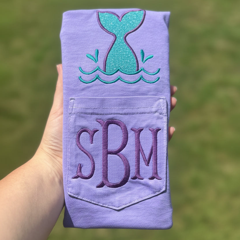 Violet Comfort Colors pocket t-shirt featuring a glitter-look embroidered mermaid tail above the pocket and personalized monogram initials stitched on the pocket, coastal beach-inspired apparel.