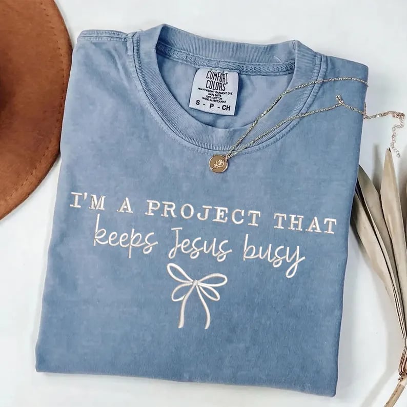 Embroidered I'm a Project That Keeps Jesus Busy Christian sweatshirt with bow design and customizable thread color.
