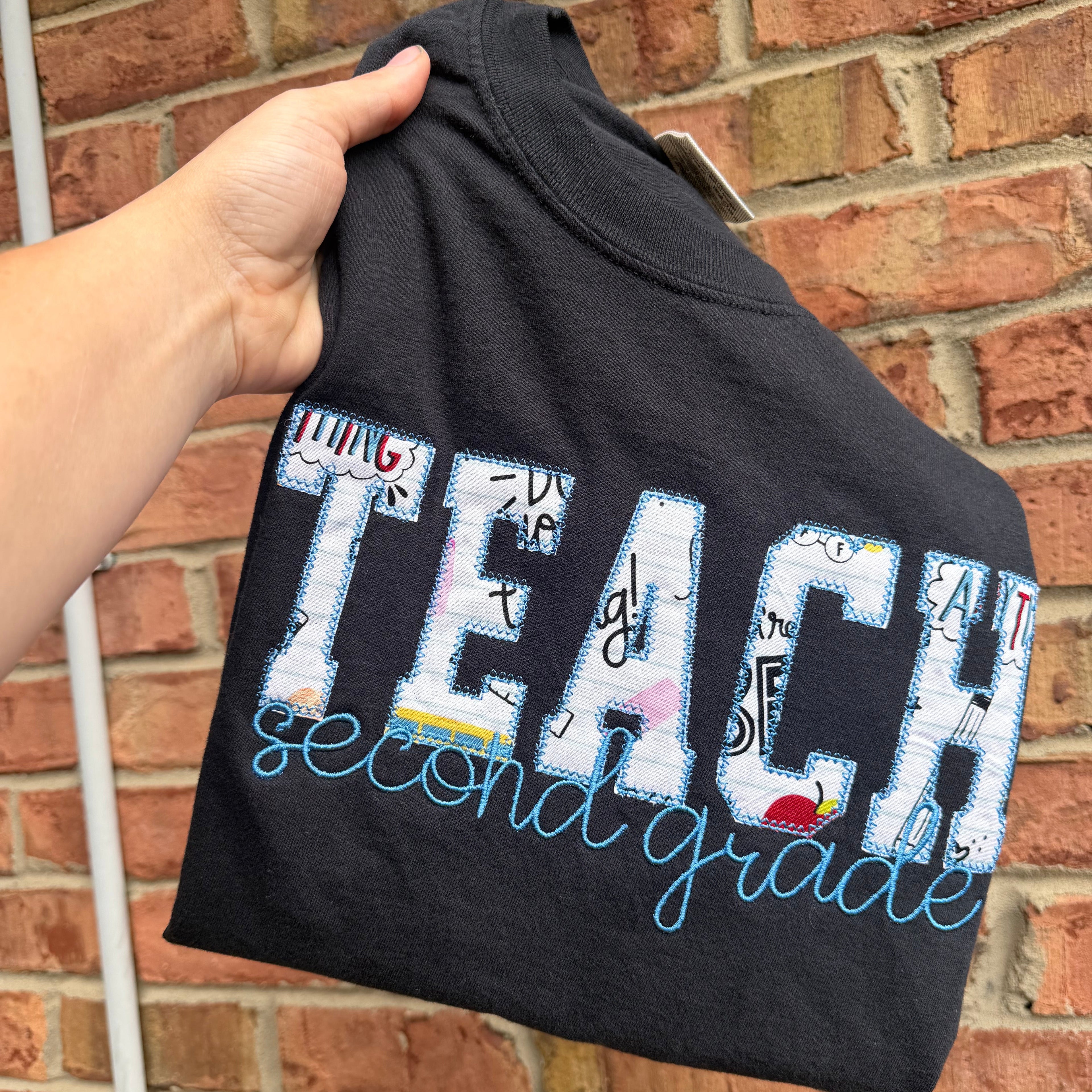 Personalized teacher appliqué shirt featuring TEACH fabric lettering with custom embroidered name underneath and customizable shirt and thread colors.