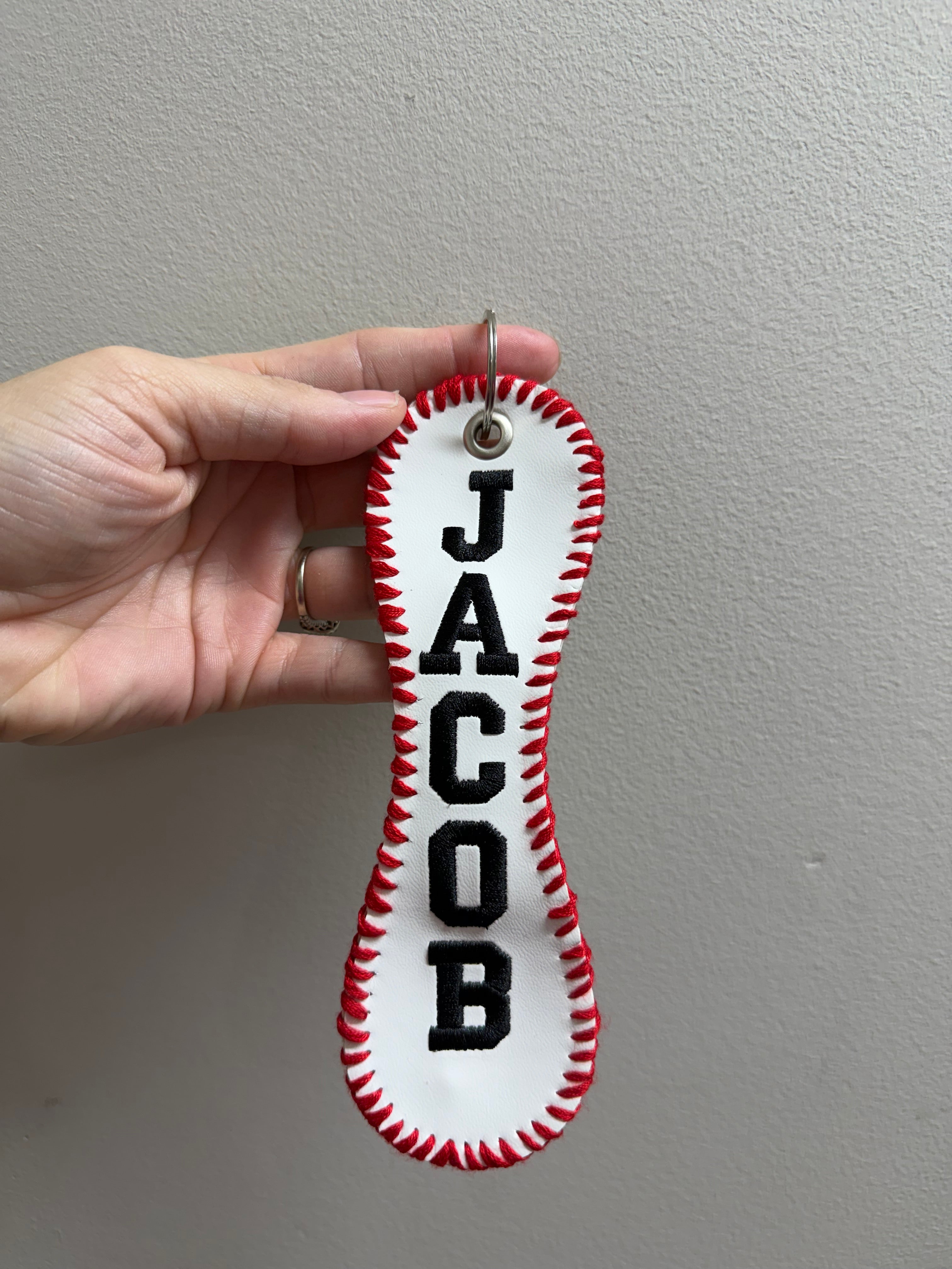 Hand holding a red and white keychain with black text against a plain background
