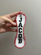 Hand holding a white keychain with red stitching and black text against a plain background