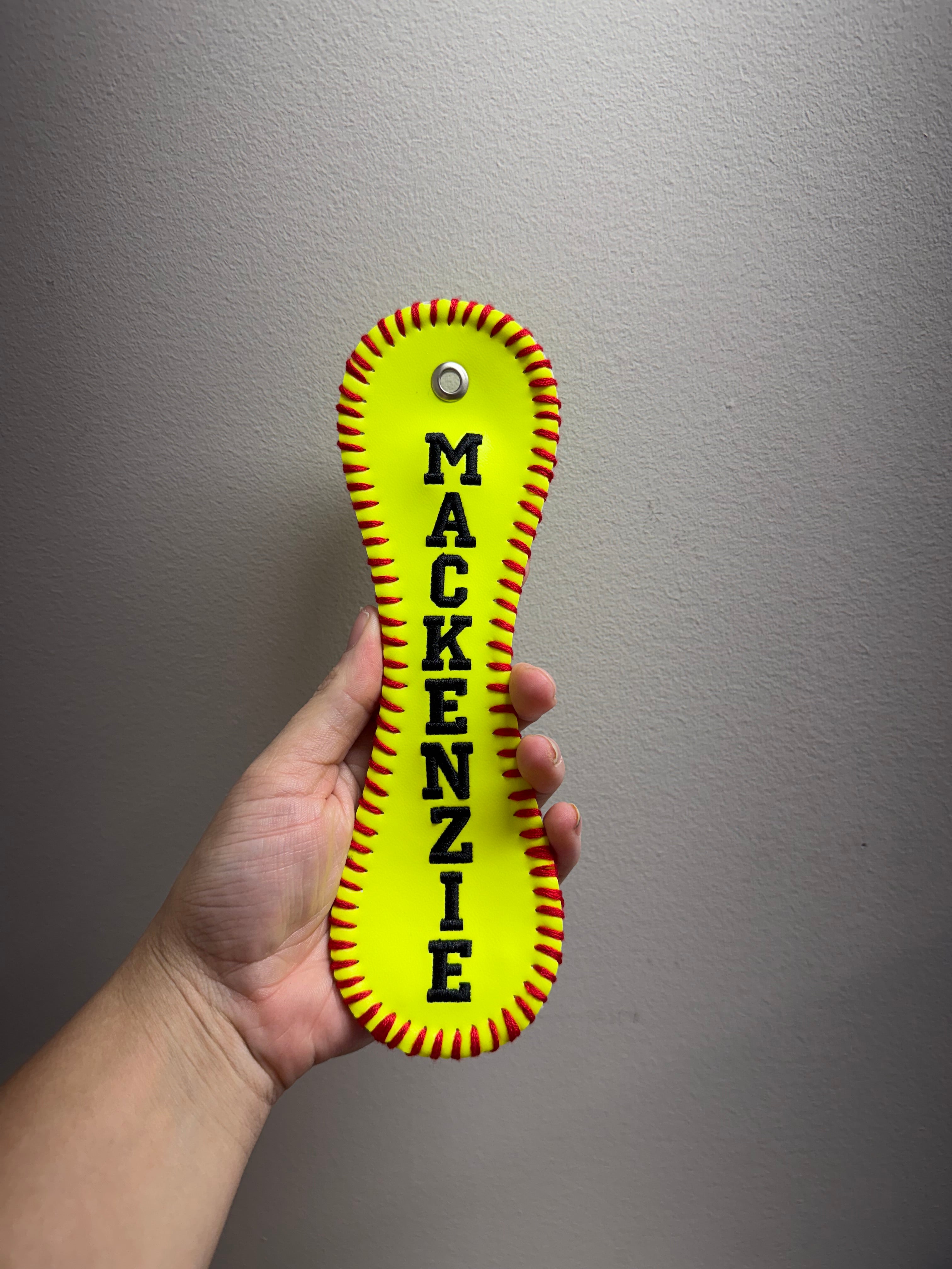 Hand holding a yellow and red dog toy with 'Mackenzie' printed on it against a gray background