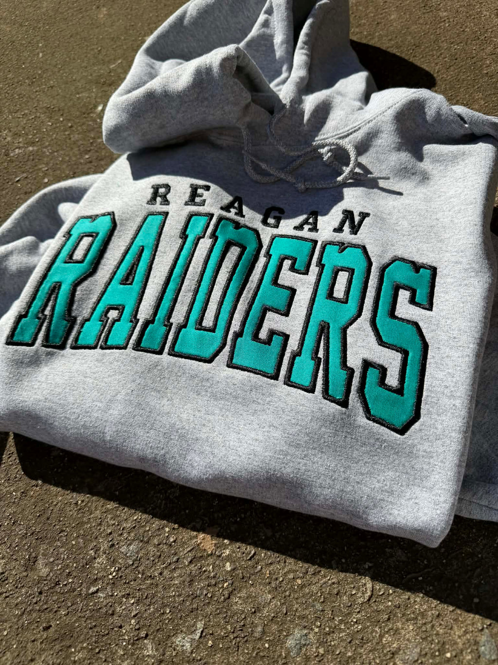 Gray hoodie with 'Reagan Raiders' text on a textured surface