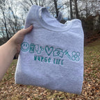 Gray embroidered nurse life sweatshirt featuring nursing-themed icons including scrubs, stethoscope, caduceus, syringe, medicine bottle, and bandages with customizable thread colors.