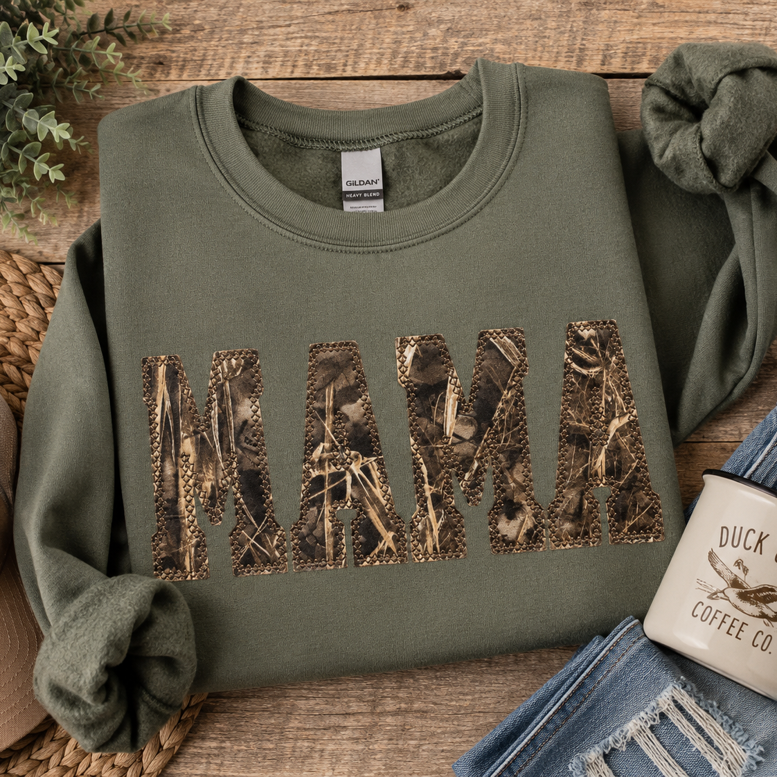Green sweatshirt with 'MAMA' in camouflage print on a wooden surface with accessories.