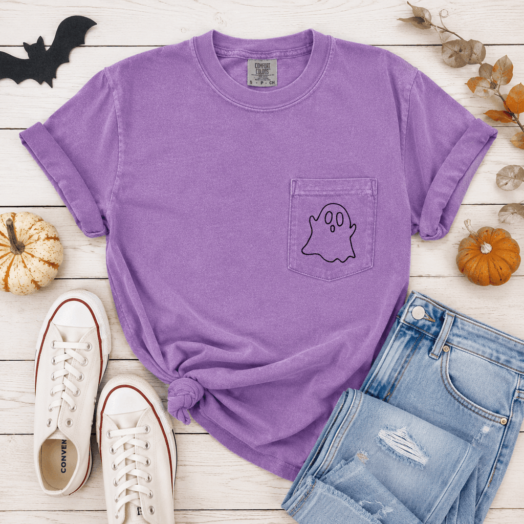Purple t-shirt with ghost design, Converse shoes, and jeans on a wooden surface with Halloween decorations.