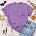 Purple t-shirt with ghost design, Converse shoes, and jeans on a wooden surface with Halloween decorations.