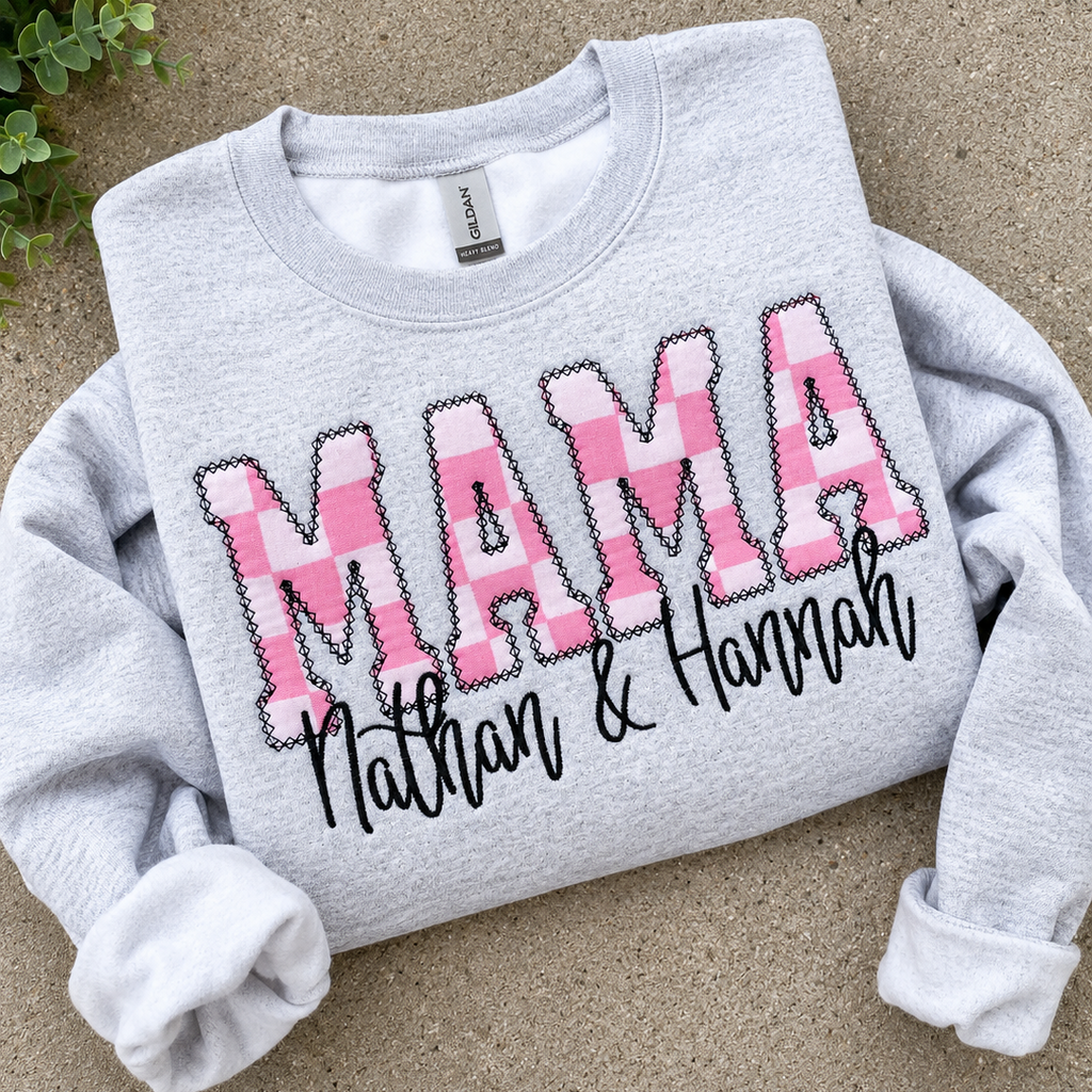 Gray sweatshirt with 'MAMA' in pink and names below on a beige surface.