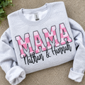 Gray sweatshirt with 'MAMA' in pink and names below on a beige surface.
