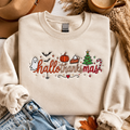 A cream-colored sweatshirt with a 'hallo thanks mas' Halloween Thanksgiving graphic, styled in a flat lay with a tan hat, blue jeans, a coffee mug, and autumn leaves on a white wood background.