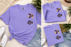 A lavender purple short-sleeve pocket T-shirt shown in a three-panel collage, styled with denim shorts, white sneakers, and a straw hat. The shirt features a chest pocket with embroidered black letters 'sBM' and a small multicolor floral graphic above it.