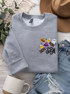 Gray embroidered Halloween sweatshirt featuring a personalized black monogram surrounded by a pumpkin, ghost, witch hat, candy corn, and Halloween candy embroidery design on the left chest.