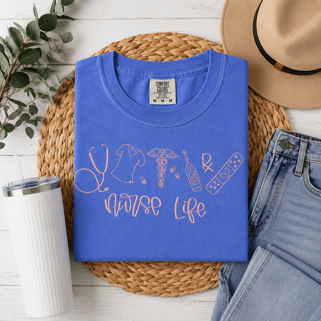Blue t-shirt with 'Nurse Life' design on a woven mat with accessories.
