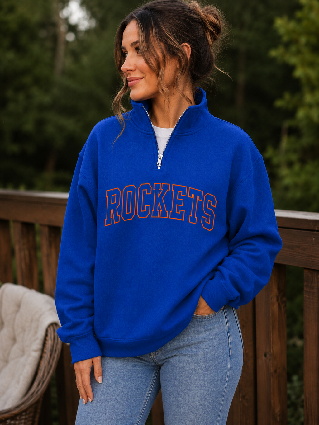 A woman wearing a royal blue quarter-zip sweatshirt with 'ROCKETS' printed across the chest in orange and white, paired with light blue jeans, standing outdoors on a wooden deck.