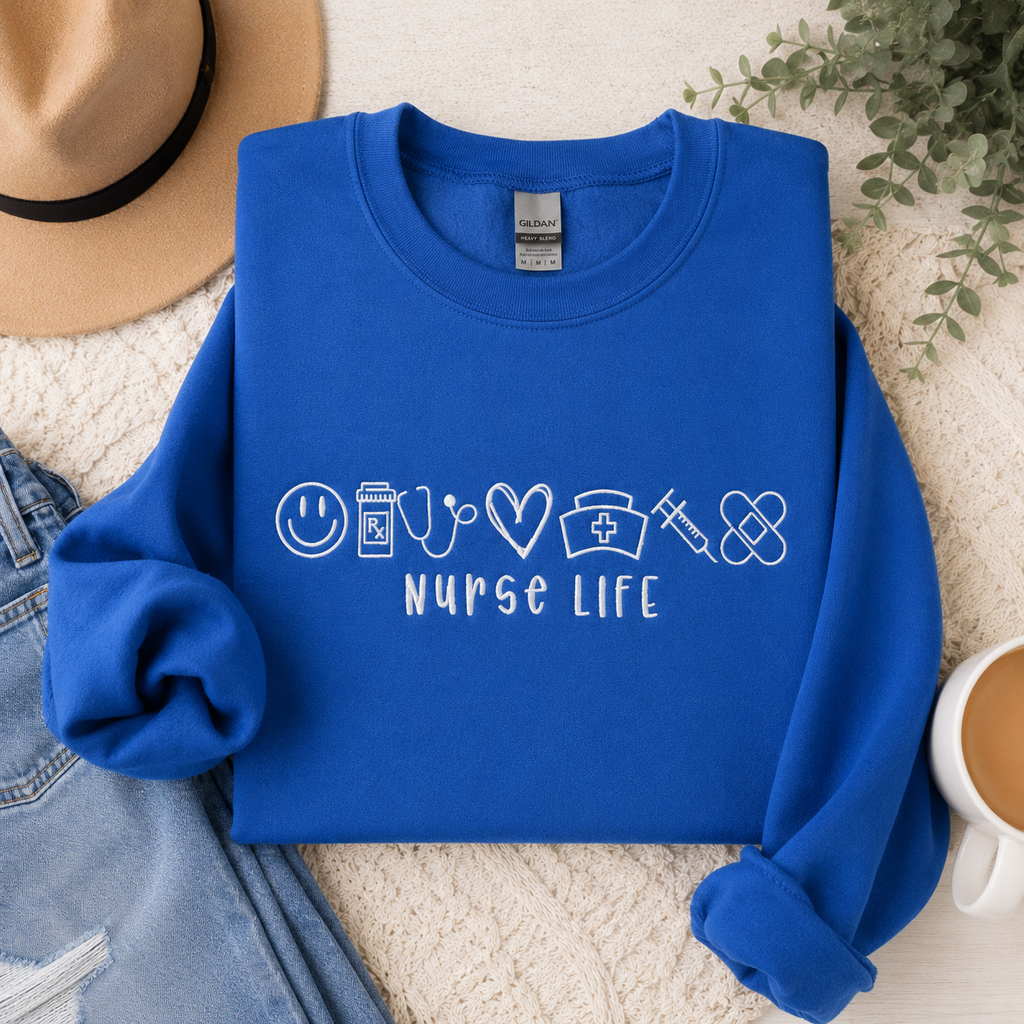 Blue sweatshirt with 'Nurse Life' design on a textured surface with a hat, jeans, and coffee cup.
