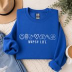 Blue sweatshirt with 'Nurse Life' design on a textured surface with a hat, jeans, and coffee cup.